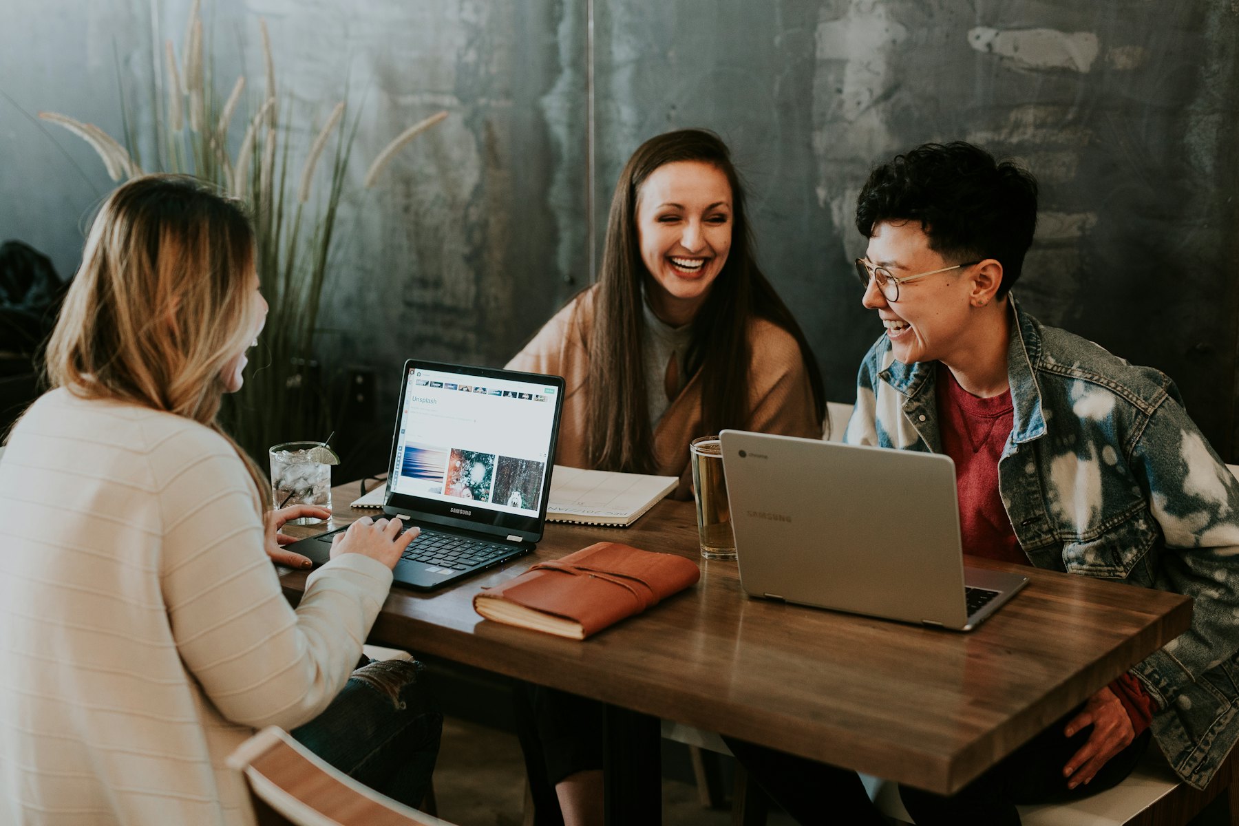 Three people laughing together at a table with a laptop