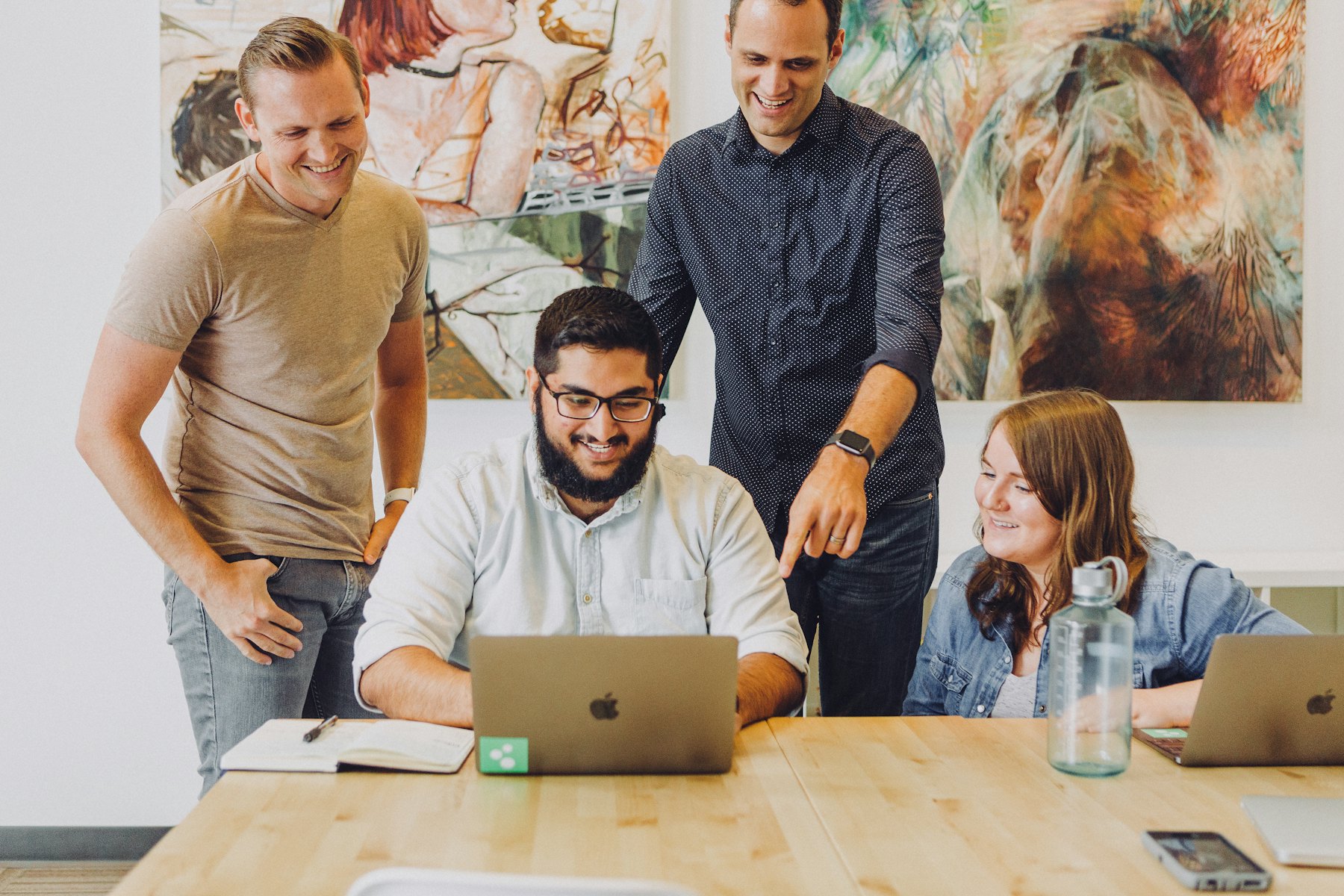 Four colleagues smiling while talking around a laptop